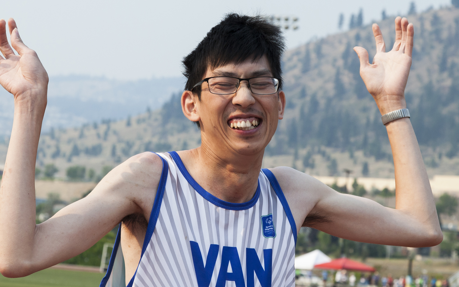 Special Olympics BC athlete with a proud smile throws his hands up in joy after his race.
