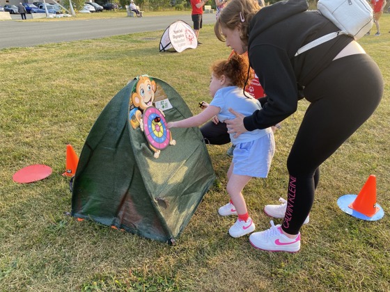 Photo taken outdoors. A little girl, being supported by her mother, is playing with a pop up toy. 