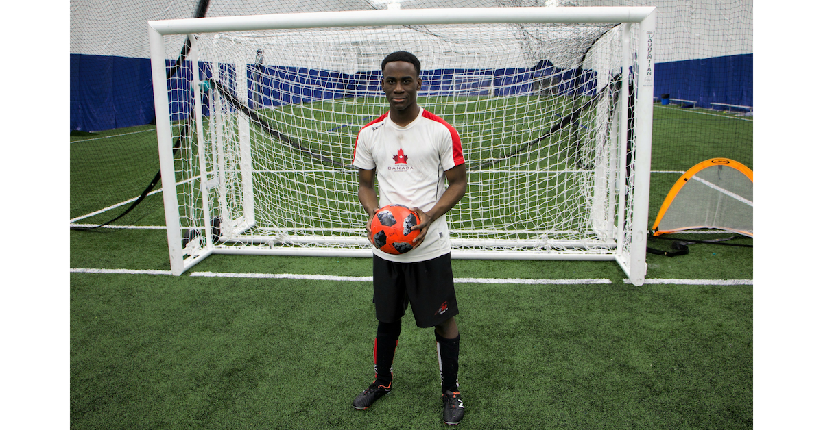 Eddie stands in front of a soccer net holding a soccer ball.
