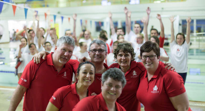 Coaches pose in front of athletes with their arms raised behind them