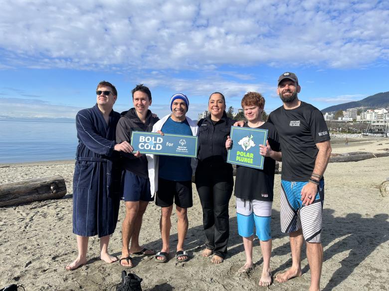 Group photo of Polar Plunge participants holding Polar Plunge signs at beach
