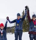 Tracey Melesko and two athletes on the podium with hands held together and raised high