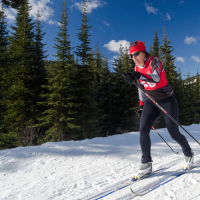 Tracey Melesko cross country skis in front of a tree line.