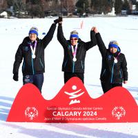 Three SO Team BC 2024 cross country skiing athletes on the podium, holding hands up together