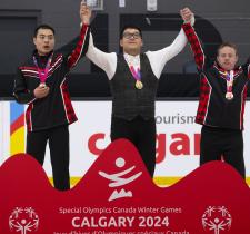 Alexander Pang standing on podium raising his hands with two other athletes