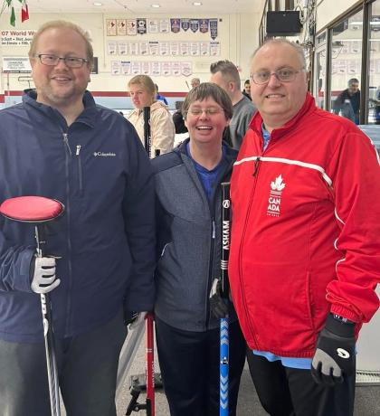Three Special Olympics curling athletes smile at the side of the rink