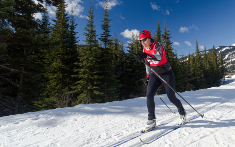 Tracey Melesko cross country skis in front of a tree line.
