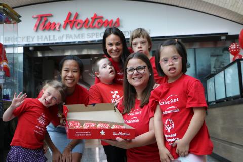 A group of young FUNdamentals athletes and their coaches stand in front of a Tim Hortons with donuts