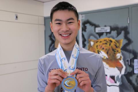 Ezekiel holds his gold medal, smiling at the camera.