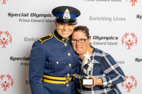 Kristi, dressed in her police uniform, poses for a photo with an athlete holding a trophy.