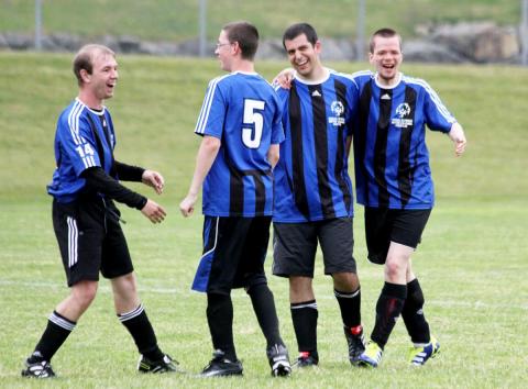 Four SOBC soccer athletes hugging each other and smiling on the field