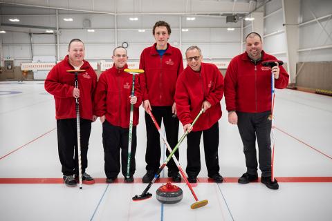 Adam poses for a photo with his curling team on the ice.