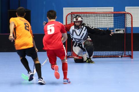 Two players and a goalie battle in floorball